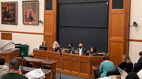 Audience seated in a classroom with panelists seated behind a table at the front of the room