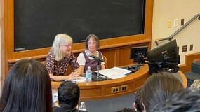 Victoria A. Cundiff ’80, left, is seated in front of a chalkboard with Roberta Romano ’80 in front of an audience of students