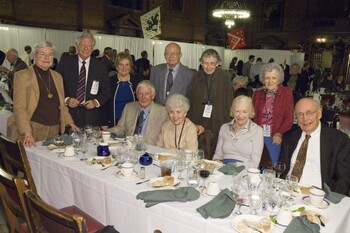 A group of alumni seated at a dinner table at a reception with more alumni standing behind them