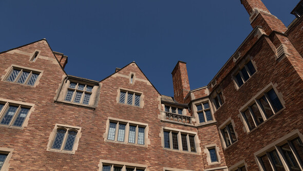 An interior-facing brick façade of Sterling Law Building with multiple pitched rooflines and stone-trimmed, leaded glass windows against a dark blue sky